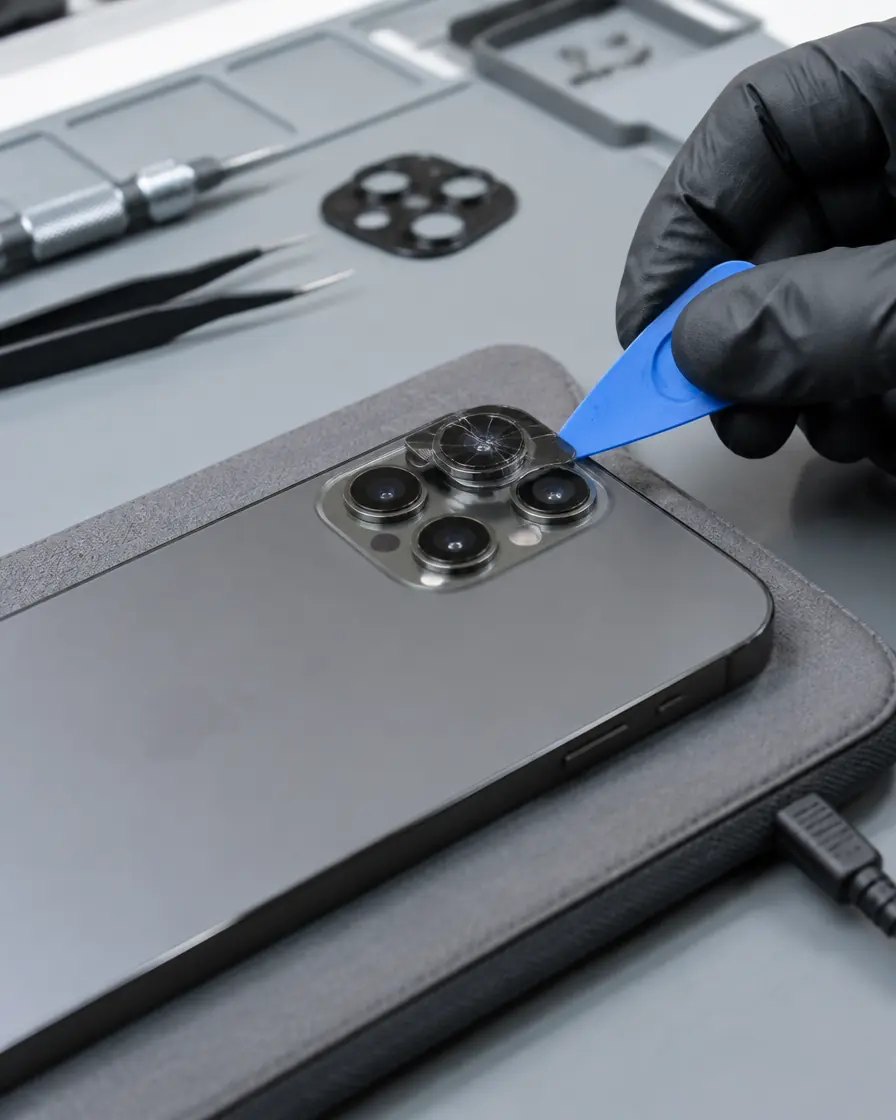 Removing a cracked camera lens from an iPhone on a heat pad during lens replacement