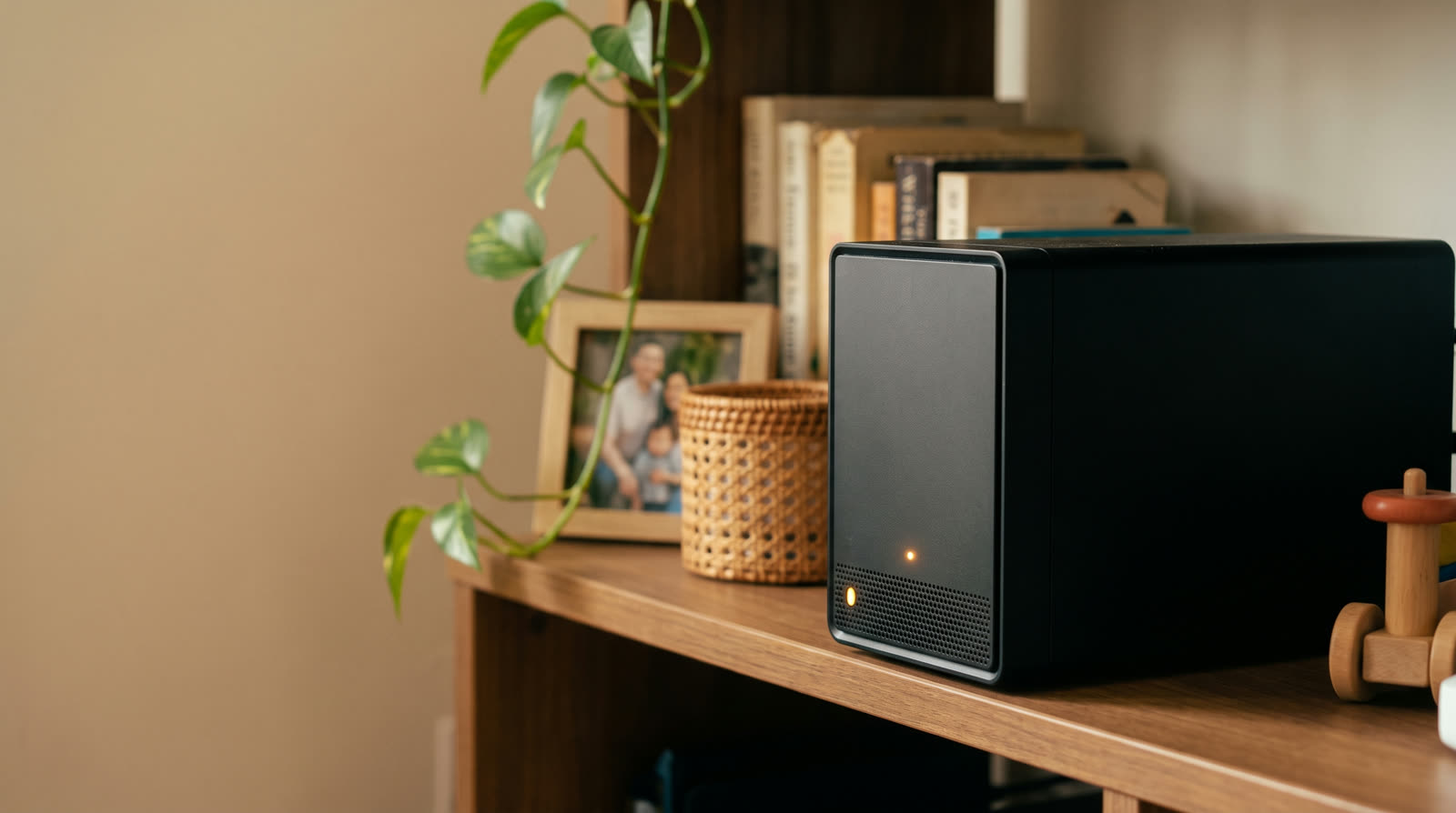 Private cloud storage box sitting on a family living room shelf beside framed photos and books, quietly backing up every phone in the house.